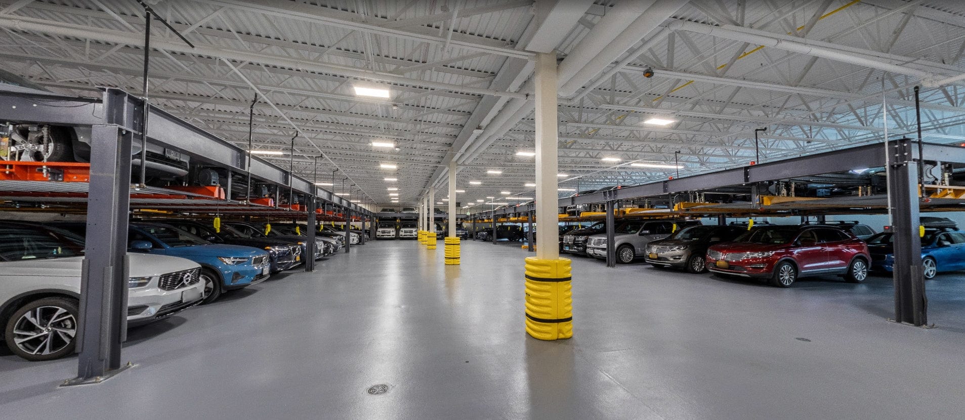 Interior of a large warehouse with cars on clear span lifts and parked vehicles.
