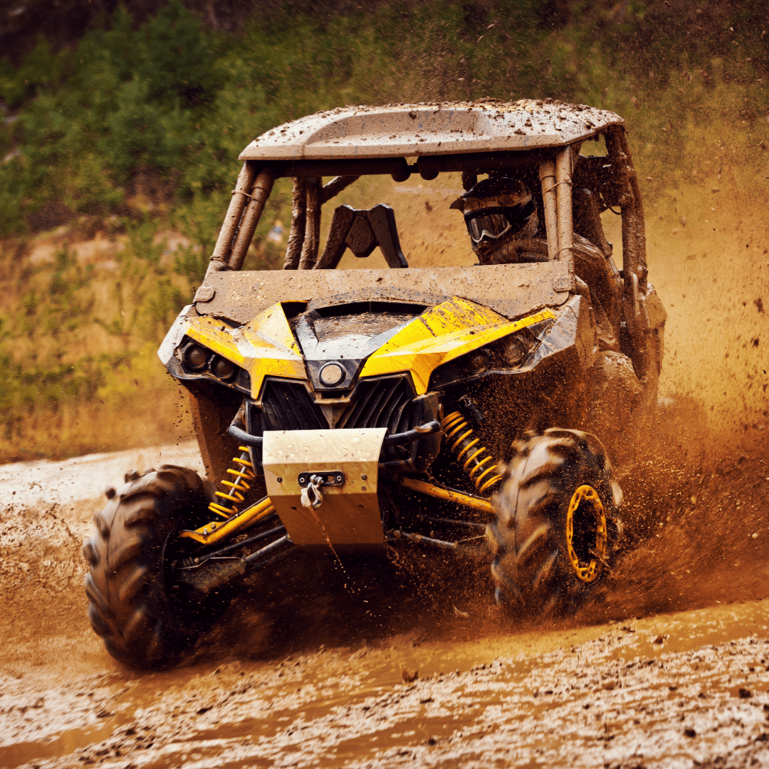 Yellow and black off-road powersports vehicle driving on a dirt path with dust in the air.